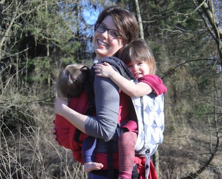 Tandemtragen, Toddlertragen, ein großes Kind ist in der Trage auf dem Rücken, ein kleines Kind wird im Tragetuch vor dem Bauch getragen.