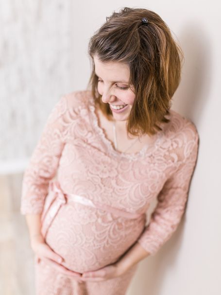 Schwangere Frau lächelt glücklich vor sich hin und hält mit beiden Händen ihren Bauch. Schwangerschaft.